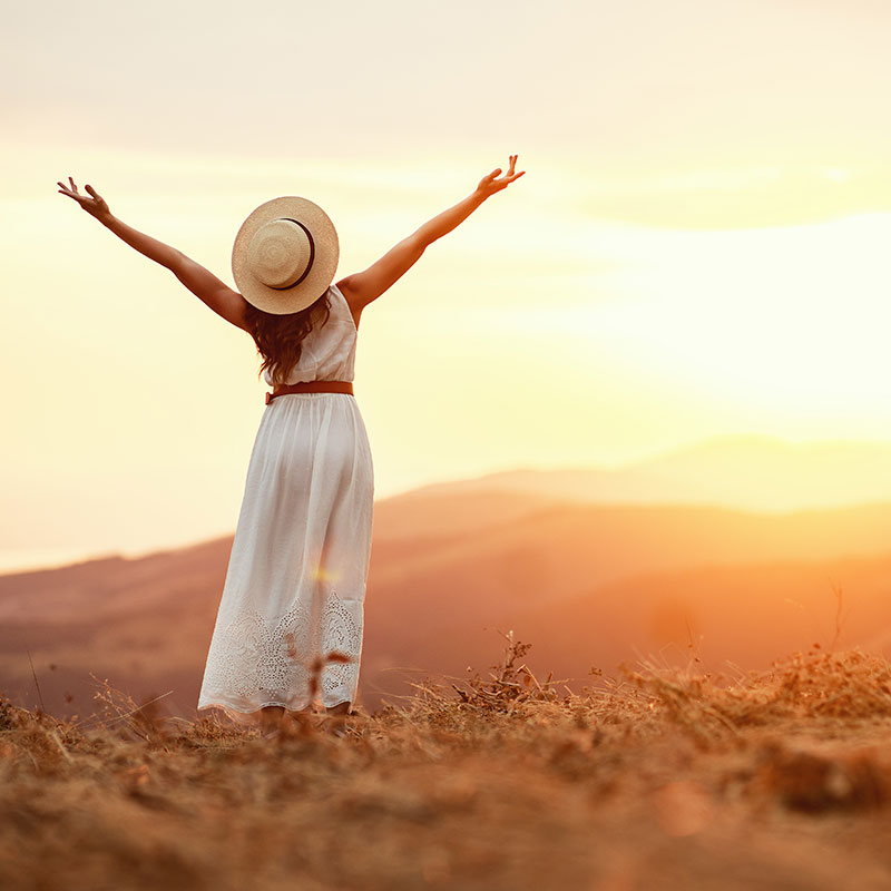 woman in white dress arms outstretched to the sunset